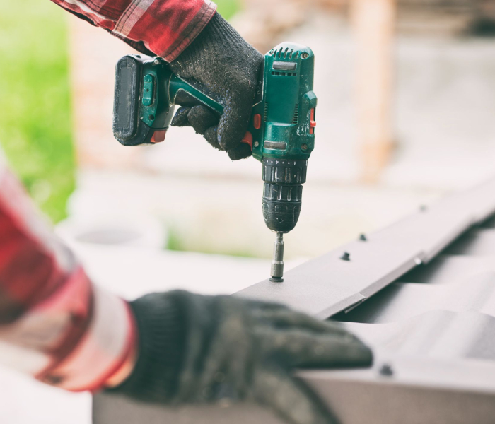 Ouvrier en gants fixant un élément de toiture avec une visseuse, pour assurer une pose précise et durable